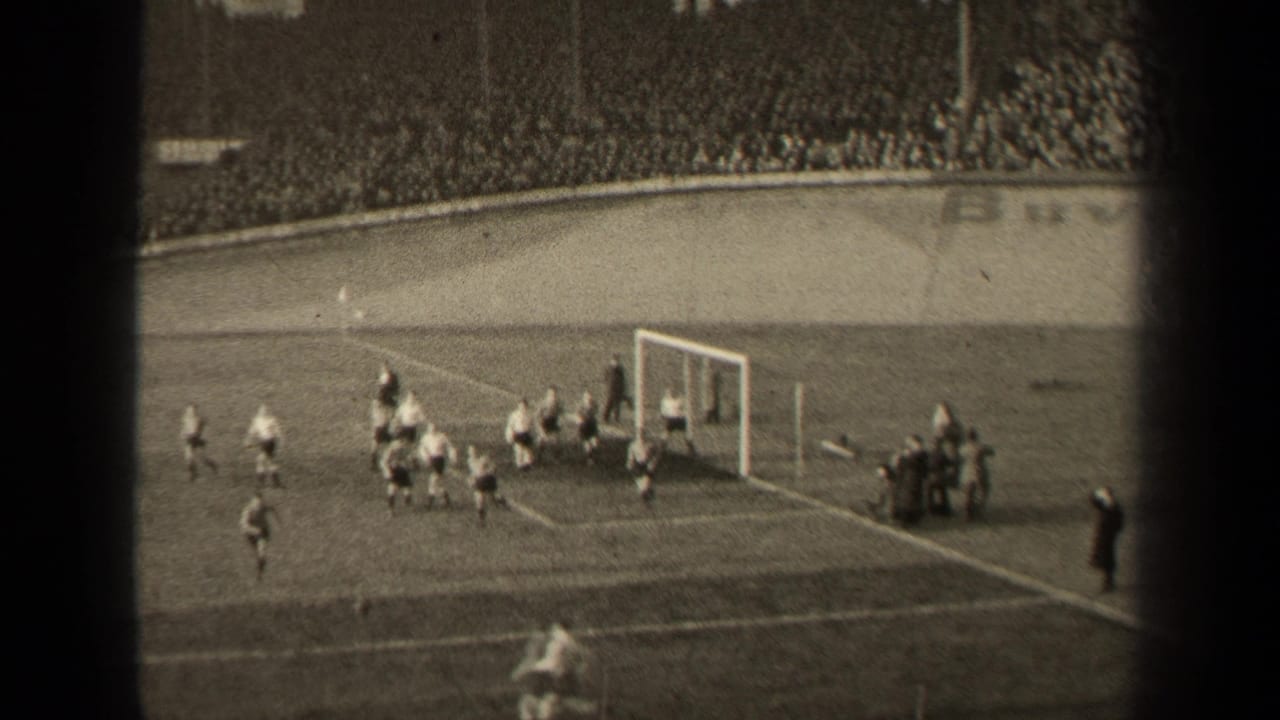 Players move around the goalmouth with spectators filling the stadium behind them.