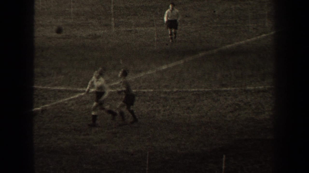 Soccer players on a grass field near marked lines, with the ball at left.