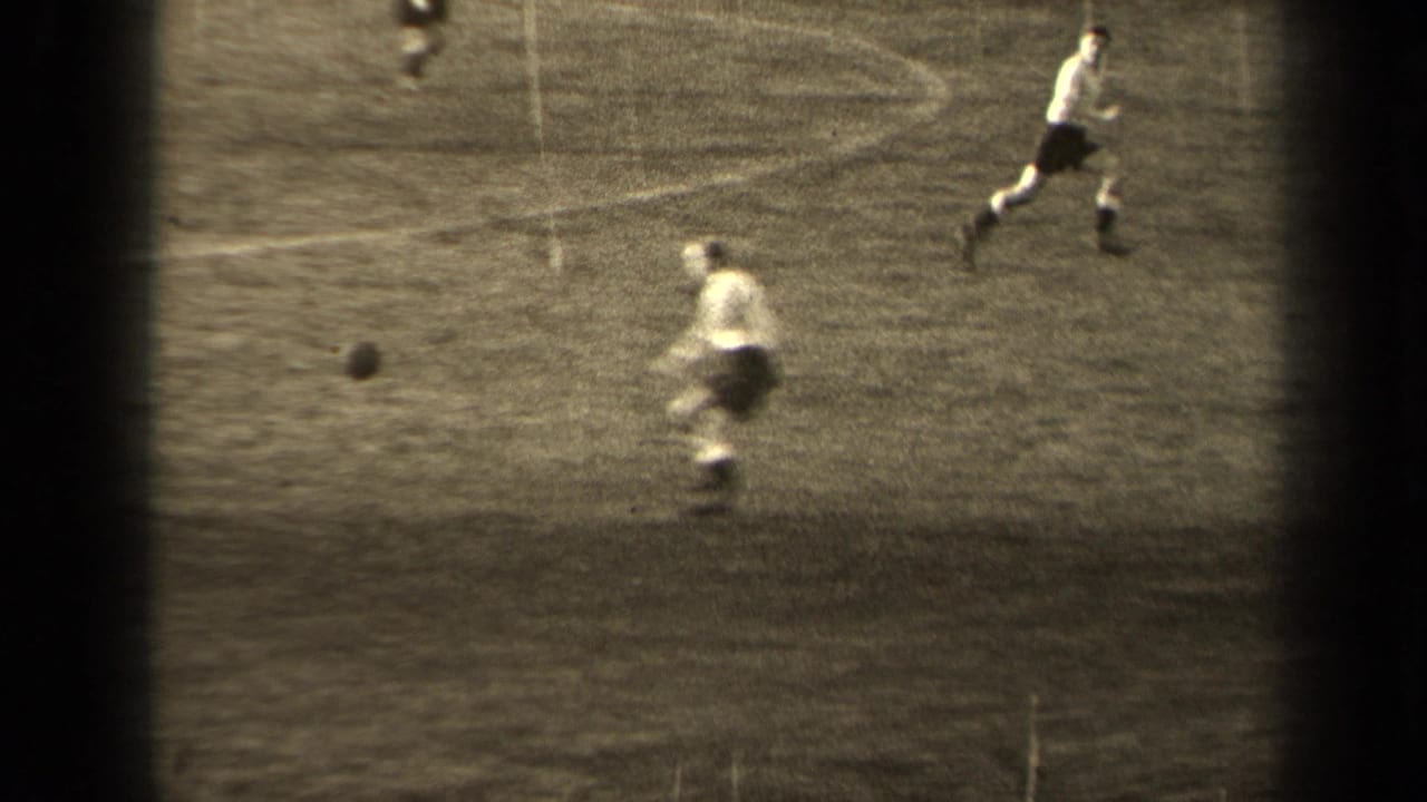A player kicks or approaches the ball while another runs across the field.