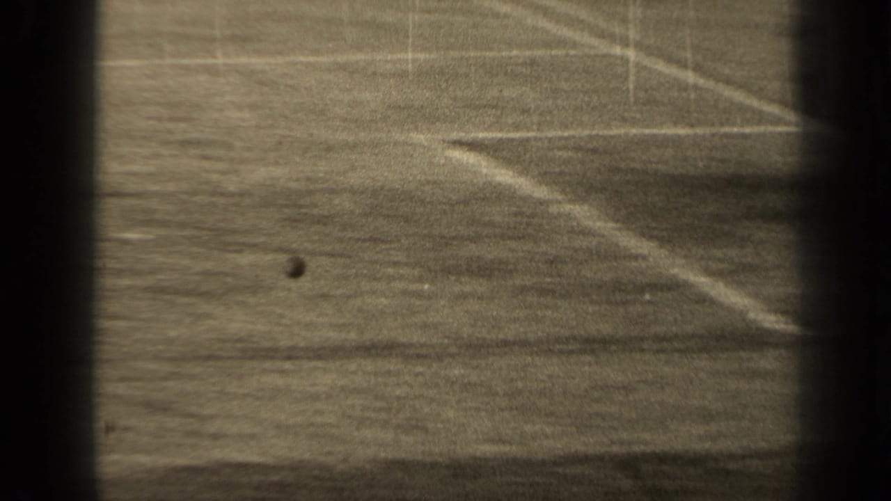 Distant football pitch seen through dark film borders with a ball on the grass.
