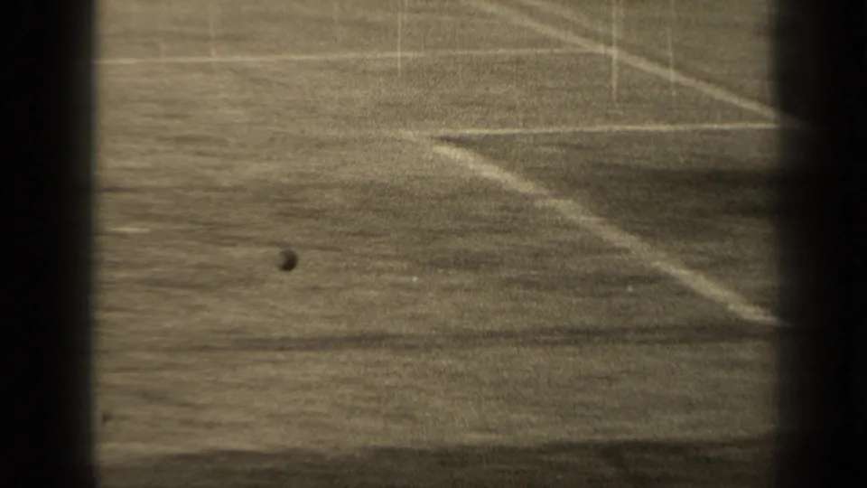 1947 Paris 8mm frame showing a marked football field from a distant spectator angle, with the ball on the grass and dark gate edges.