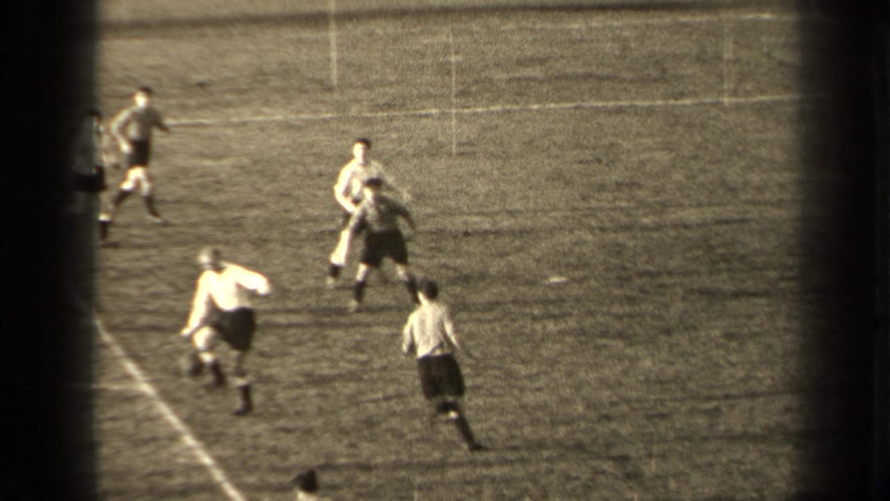 Players in white and dark uniforms compete for a soccer ball on a grass field.