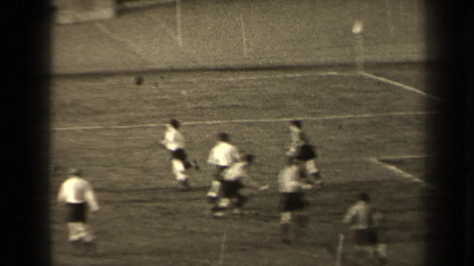 The match continues as players in light and dark kits run across the grass, with the ball visible above the group.