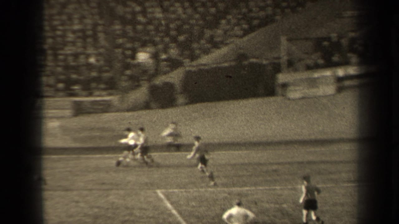 Players challenge for the ball near the edge of the penalty area in a stadium.