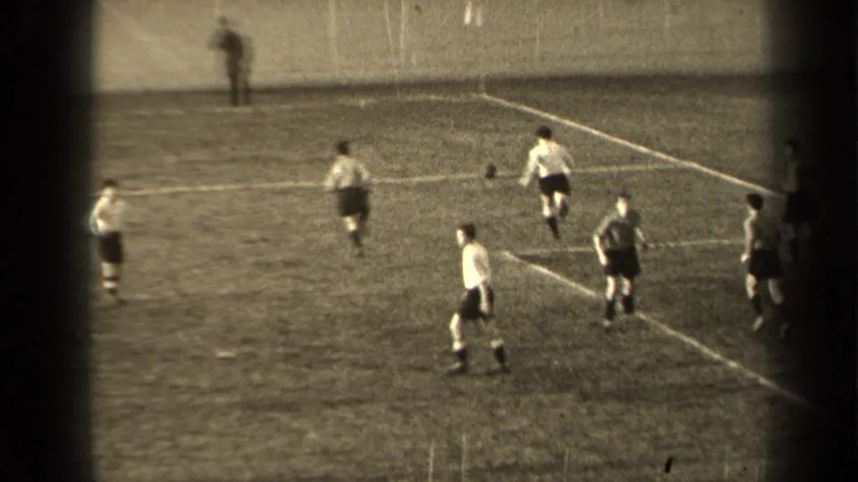 Wide 1947 Paris frame of a football match, with players positioned across the pitch and a wall beyond the field.