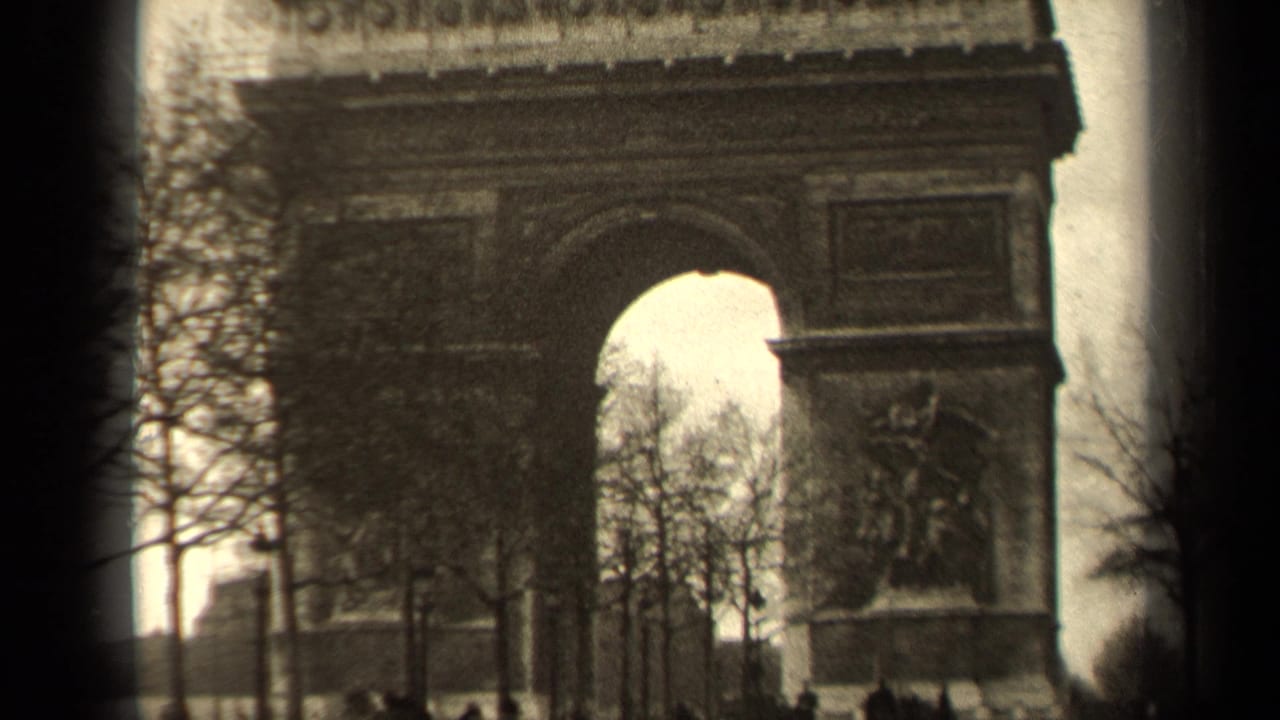 Arc de Triomphe seen through bare trees with small pedestrians near the street edge.