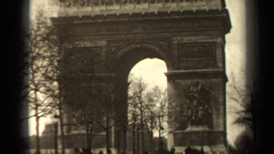 1947 Paris home-movie frame showing the Arc de Triomphe, bare trees, and small pedestrian figures in front.