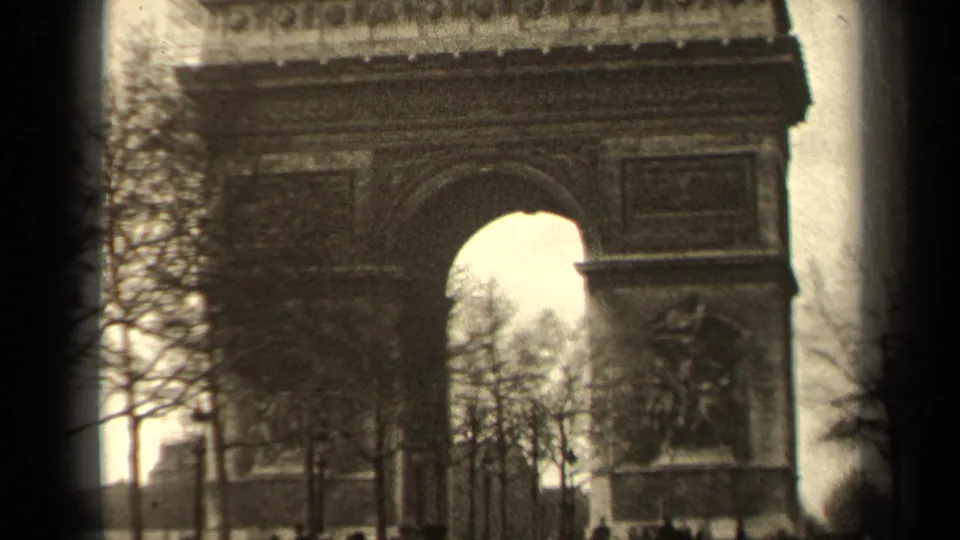 1947 Paris frame with the Arc de Triomphe facade, sculptural panel, bare trees, and pedestrians near the base.