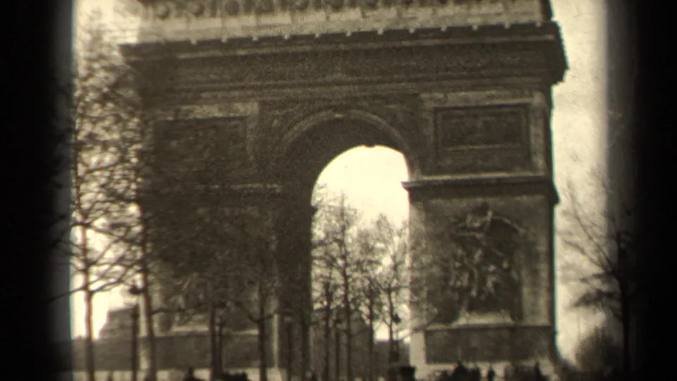 1947 Paris home-movie view of the Arc de Triomphe with pedestrians, bare trees, and the arch opening visible.