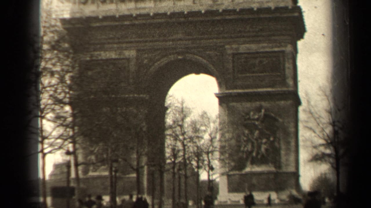 1947 8mm view of the Arc de Triomphe in Paris, framed by winter trees and small pedestrian figures near the street level.
