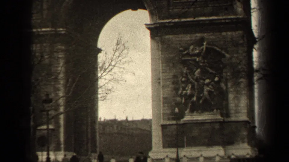 1947 8mm view of the Arc de Triomphe in Paris, framed by dark film edges with bare trees and distant pedestrians near the base.