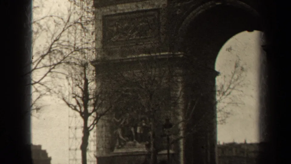 End frame of 1947 Paris 8mm footage showing the Arc de Triomphe arch, sculptural relief, bare trees, street lamps, and small pedestrians.