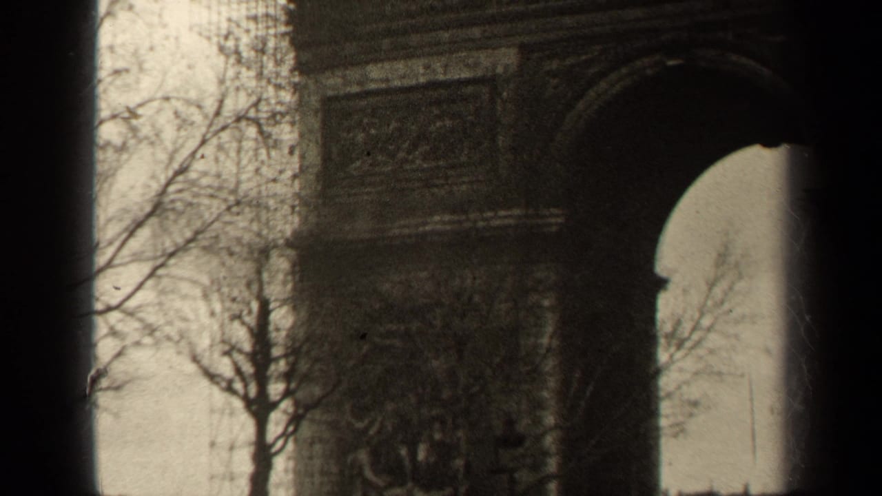 1947 Paris 8mm frame showing part of the Arc de Triomphe arch, stone reliefs, bare trees, and cloudy sky.