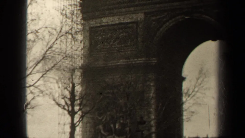1947 Paris 8mm frame showing part of the Arc de Triomphe arch, stone reliefs, bare trees, and cloudy sky.