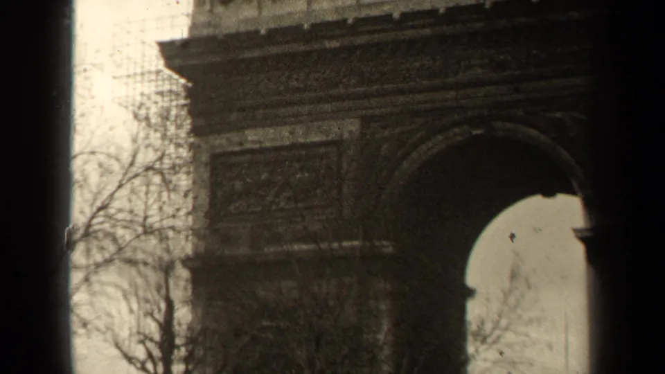 1947 Paris frame with the Arc de Triomphe arch, sculpted facade, bare trees, cloudy sky, and visible 8mm gate shadows.