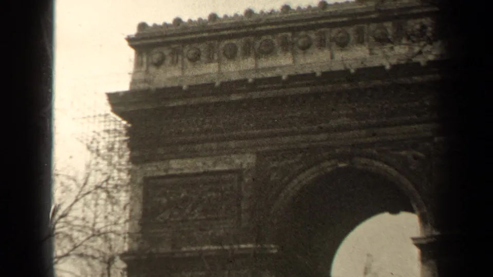 1947 Paris 8mm frame showing the upper Arc de Triomphe stonework and arch, framed by bare branches and dark film edges.
