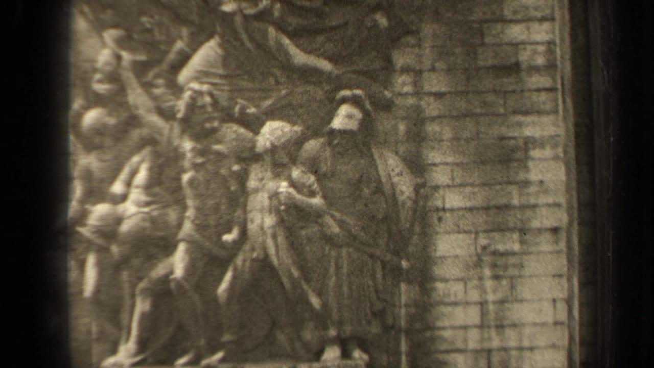 1947 Paris home-movie frame showing a close portion of a stone bas-relief with draped carved figures and masonry behind it.