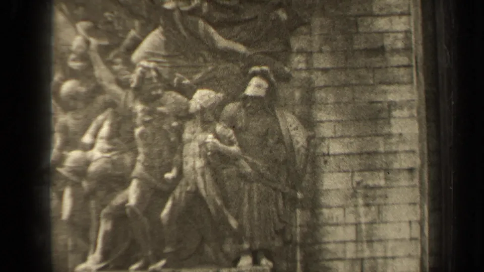 1947 Paris home-movie frame showing a close portion of a stone bas-relief with draped carved figures and masonry behind it.
