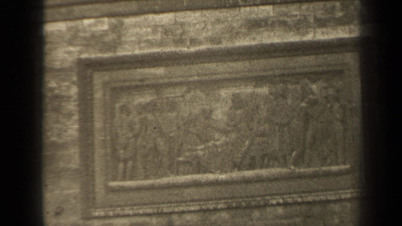 Framed relief panel with faint figures on an aged metal or stone surface.