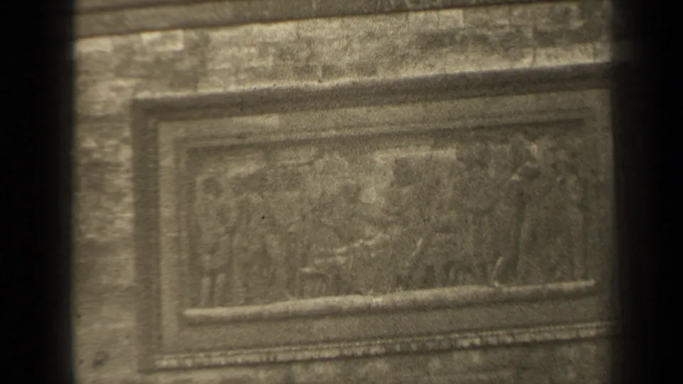 Close 8mm view in Paris of a rectangular relief panel with faint human figures and tarnished surface texture.