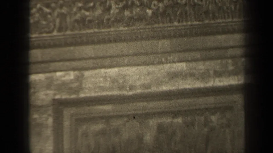 Close 8mm Paris view of a partial bas-relief panel below a decorative band, with tarnished material and soft focus.