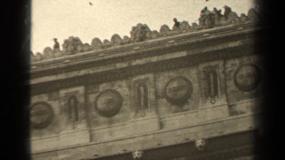 1947 Paris 8mm frame showing a tilted close-up of historic stone facade ornament with circular reliefs and upper cornice detail.