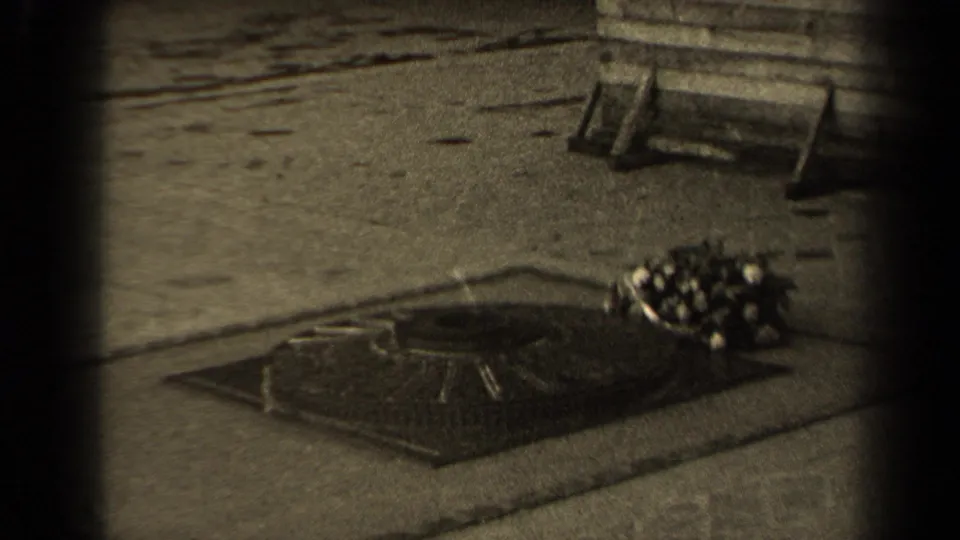 1947 Paris 8mm frame with a ground-level memorial feature, nearby bouquet, stone pavement, and bench-like object in the background.
