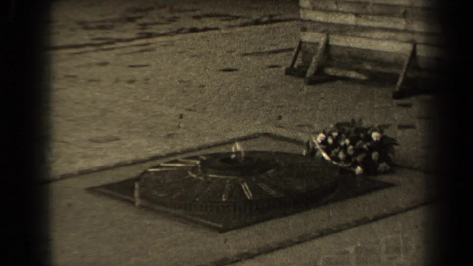 1947 Paris 8mm frame showing the memorial flame surround and flowers beside it, with paving and a bench-like form behind.