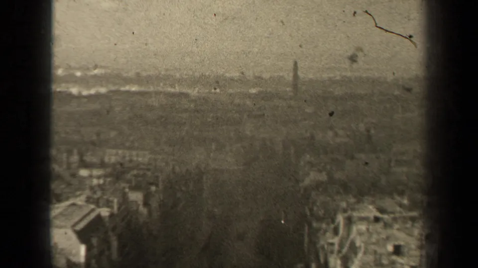 Paris, France metadata-supported city view on 8mm film, with dense rooftops, trees, haze and a distant spire visible through wear.