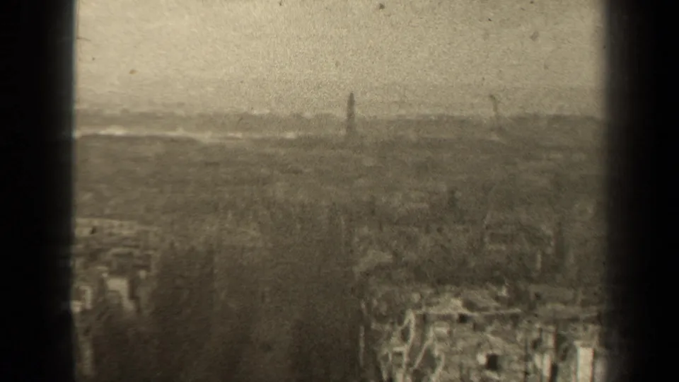 Hazy 1947 Paris cityscape frame with rooftops below, tree cover and a tall distant structure, partly obscured by grain and scratches.