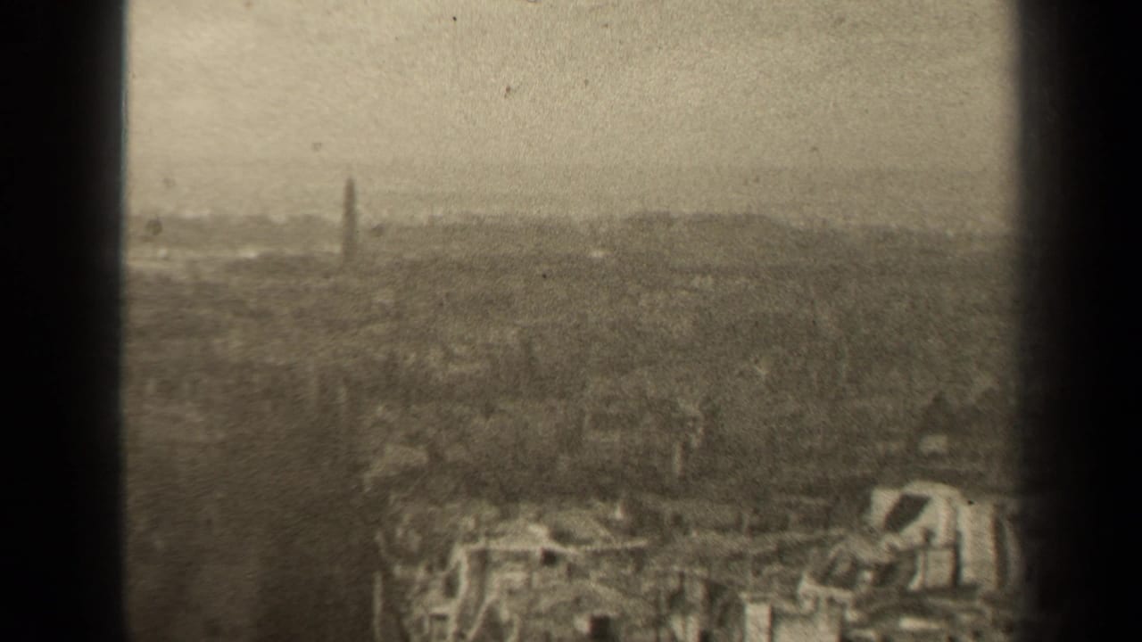 Soft skyline view with dense buildings, distant tower, haze, and visible film wear.