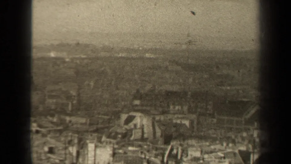 Grainy 8mm frame of a likely 1947 Paris ruin scene, showing damaged low buildings, scattered debris, and distant rooftops.