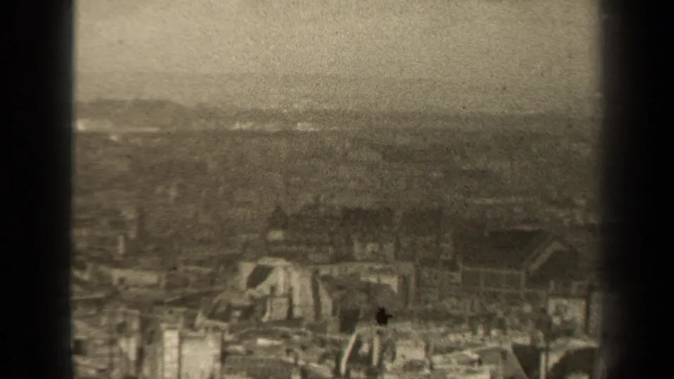 A 1947 Paris-linked home-movie frame shows rubble, damaged structures, rooftops, and a distant hazy landscape from above.