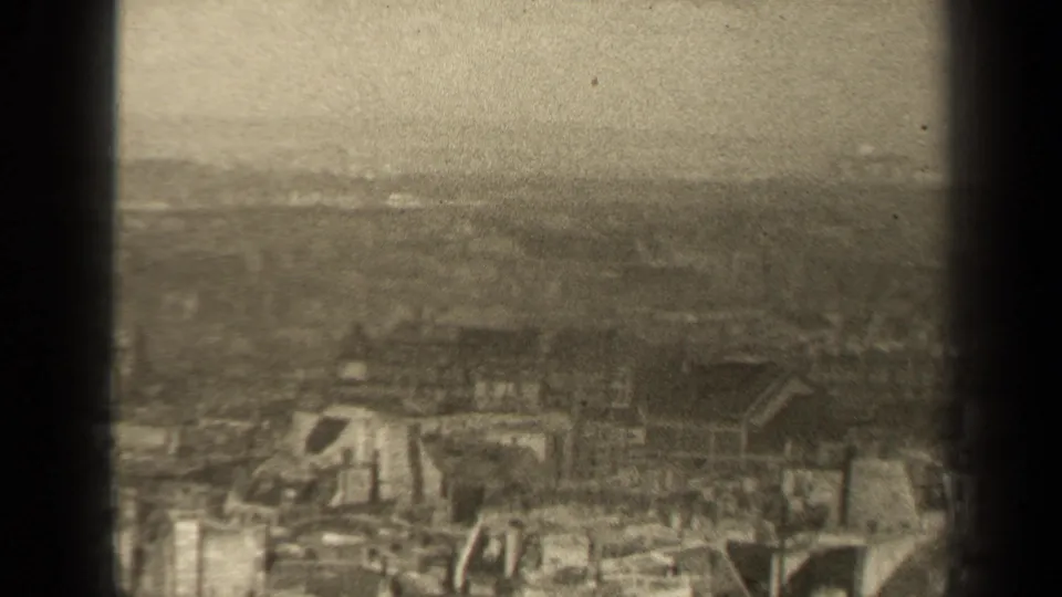 Final 8mm still from the supplied 1947 Paris clip, with ruined structures in the foreground and a broad hazy city horizon beyond.