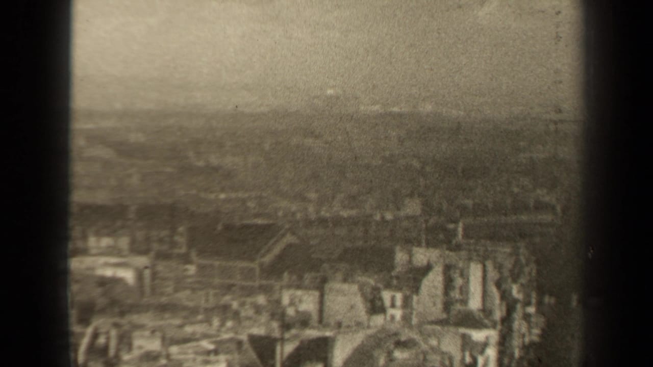 Hazy elevated view of dense old town rooftops seen through dark vertical frame bars.