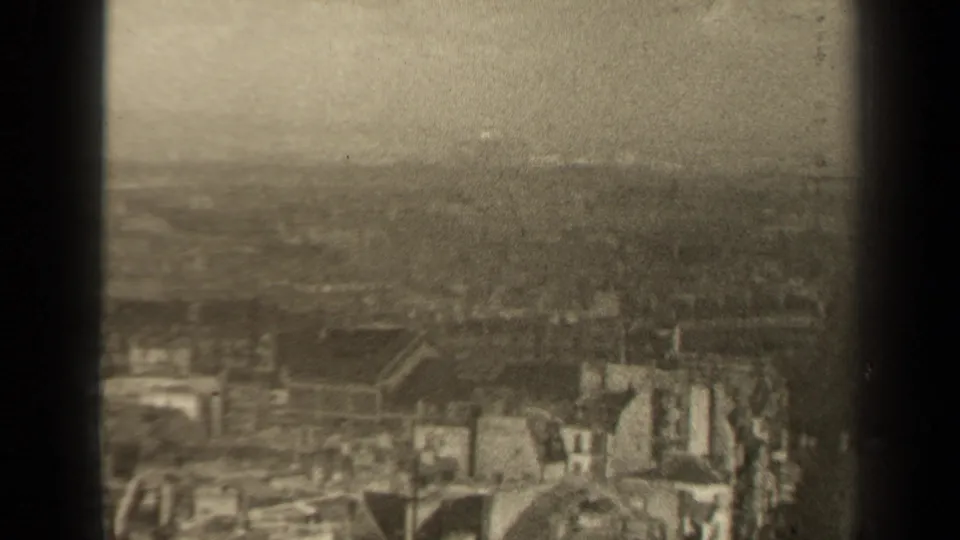 1947 Paris home-movie frame showing a soft, high-angle view over dense rooftops and light building facades through dark foreground bars.