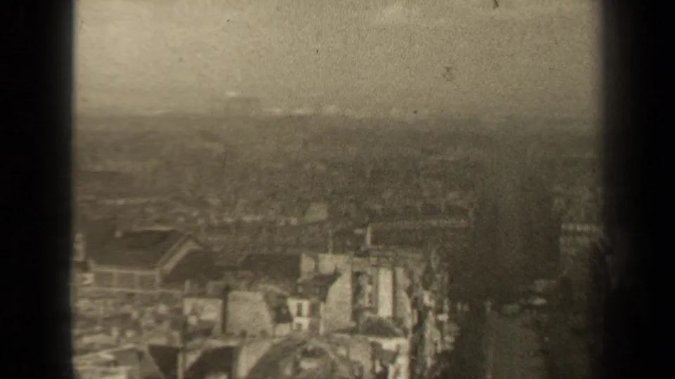 Soft 1947 Paris 8mm frame looking over older rooftops and building fronts, with haze and a dark vertical divider in the foreground.