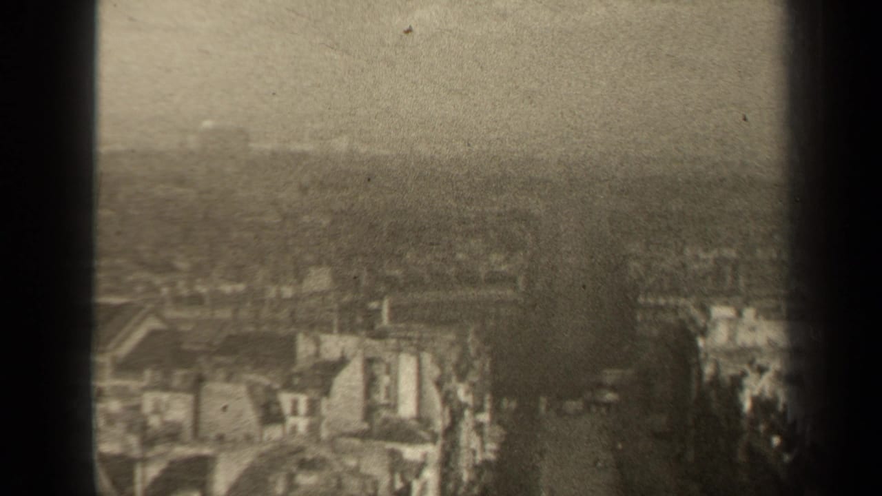 1947 8mm high-angle view over Paris rooftops and streets, with distant horizon and soft overcast exposure.