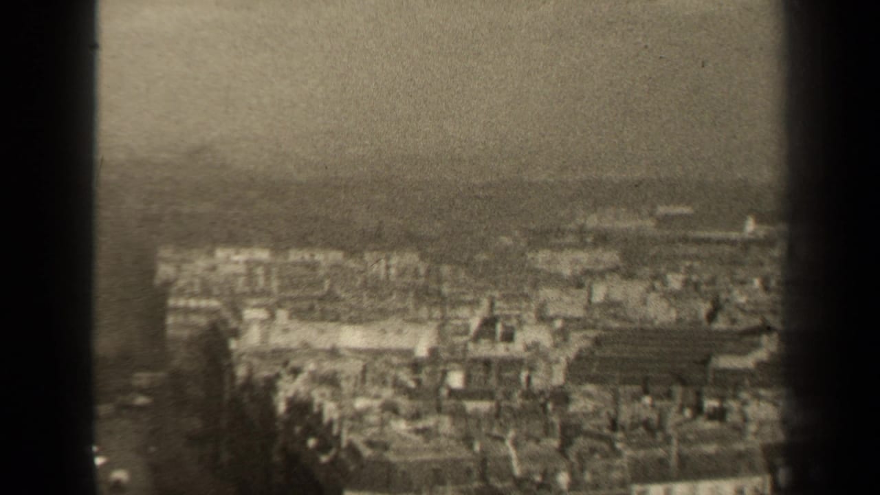 1947 Paris home-movie frame showing a hazy elevated view across dense rooftops and low buildings, with dark 8mm frame borders.
