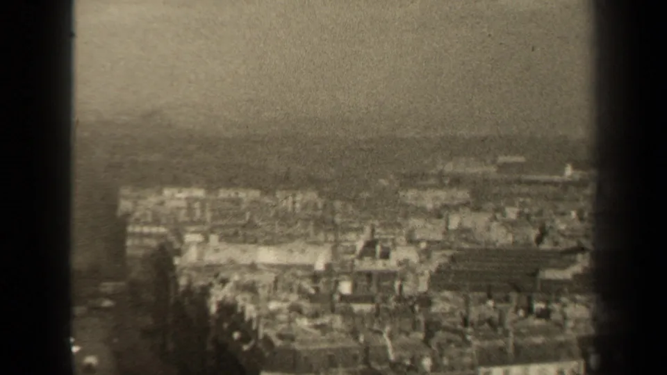 1947 Paris home-movie frame showing a hazy elevated view across dense rooftops and low buildings, with dark 8mm frame borders.