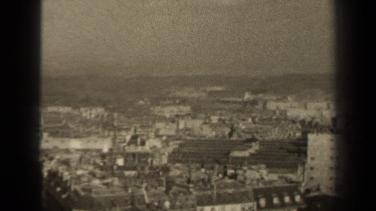Distant urban panorama with rooftops, haze, and a dark center film border.