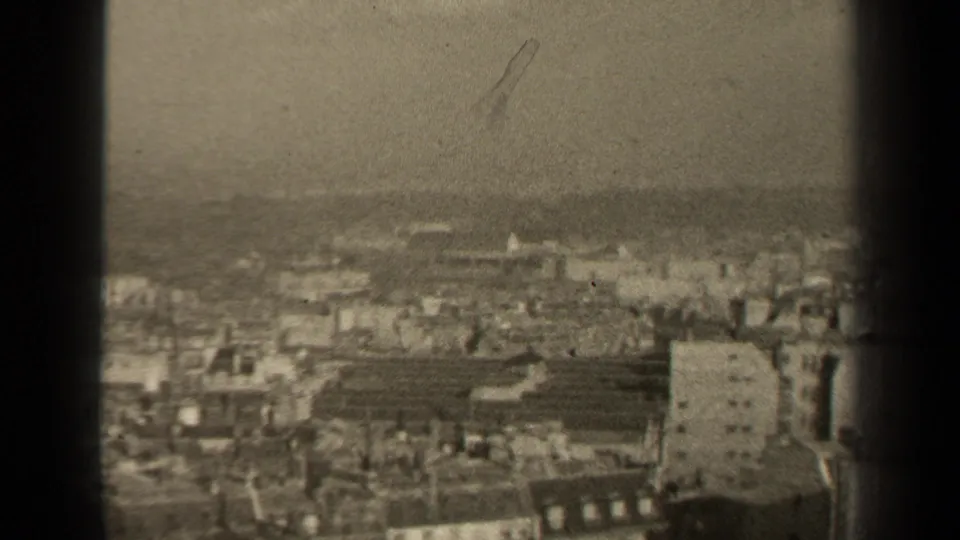 Elevated 1947 Paris view with low rooftops, blocky foreground buildings, haze, and visible 8mm grain across the frame.
