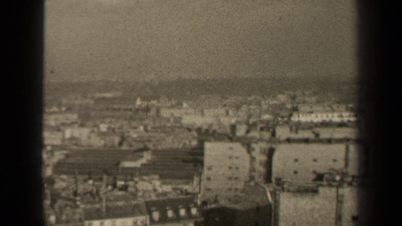 1947 8mm high-angle view over Paris rooftops and dense buildings, framed by dark vertical edges.