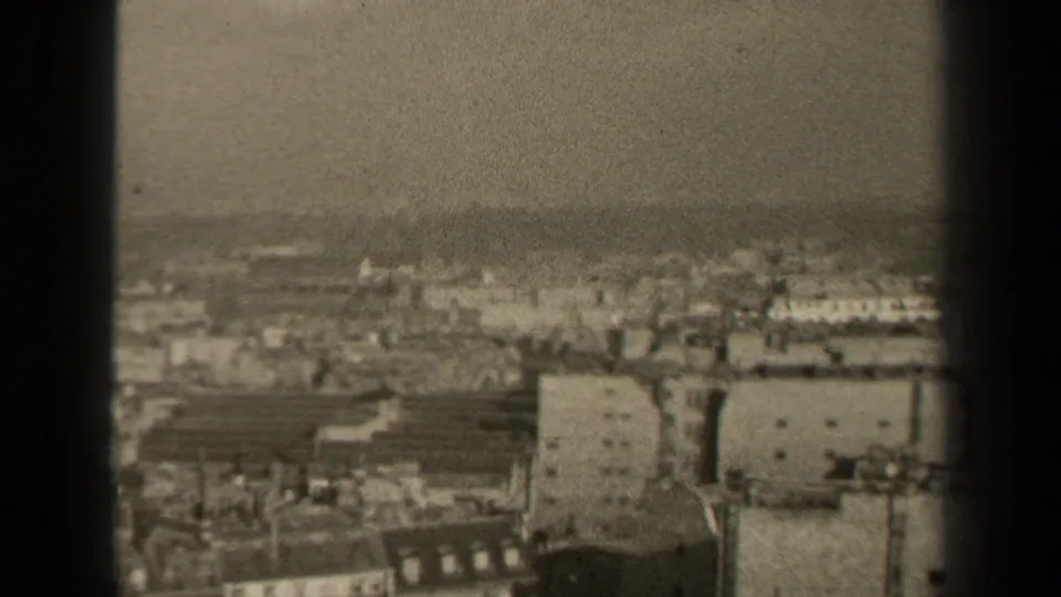 1947 8mm high-angle view over Paris rooftops and dense buildings, framed by dark vertical edges.