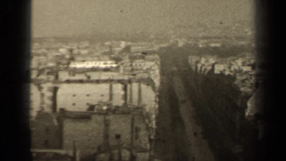 High-angle 8mm frame showing a broad Paris street cutting through rooftops and dense urban blocks.
