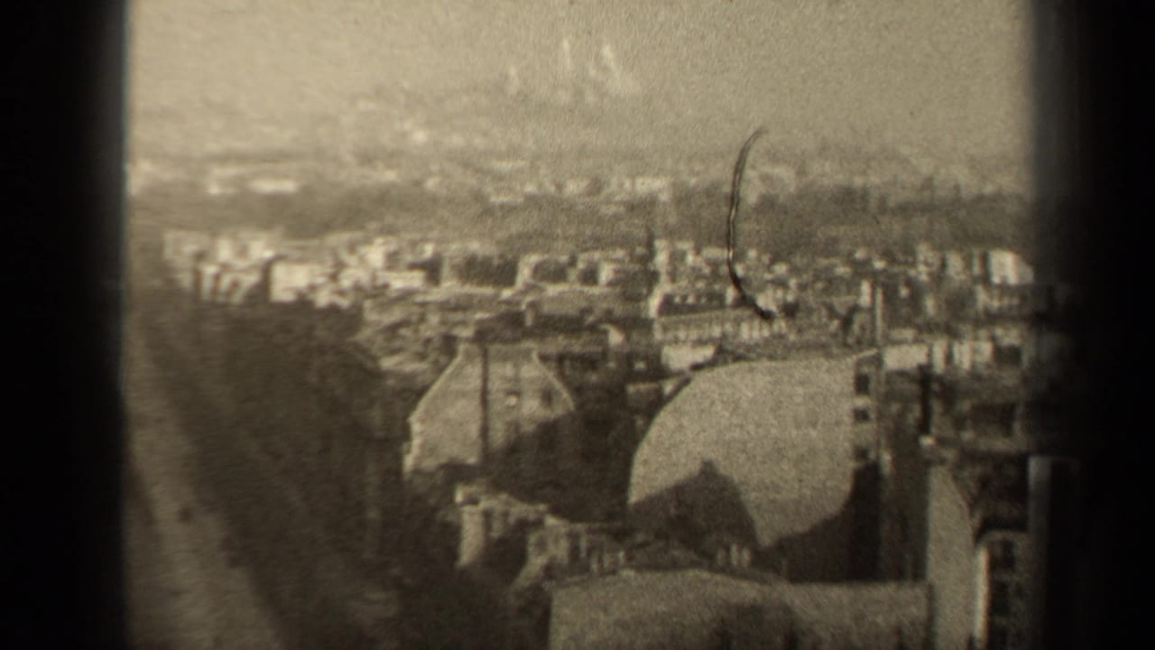 1947 Paris home-movie frame showing an elevated city panorama with rooftops, a domed form, distant spires, grain, and scratches.