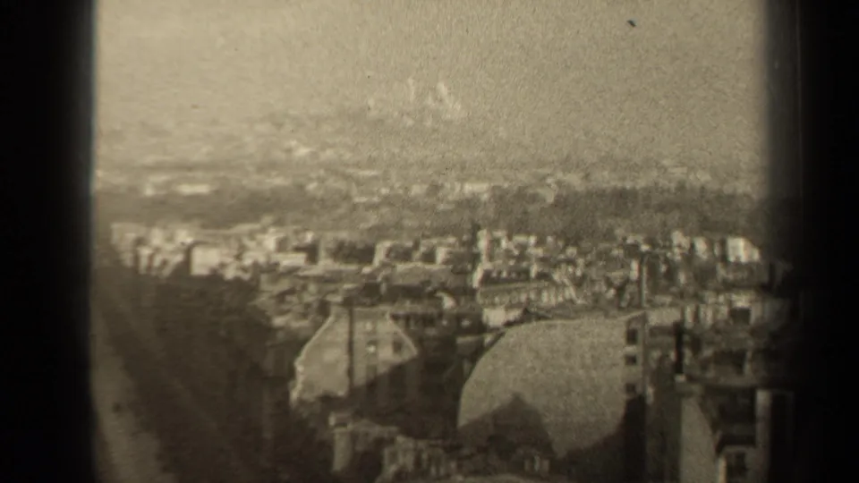 1947 Paris elevated view showing layered rooftops, a domed mid-ground structure, dark film gate edges, scratches, and a hazy background.