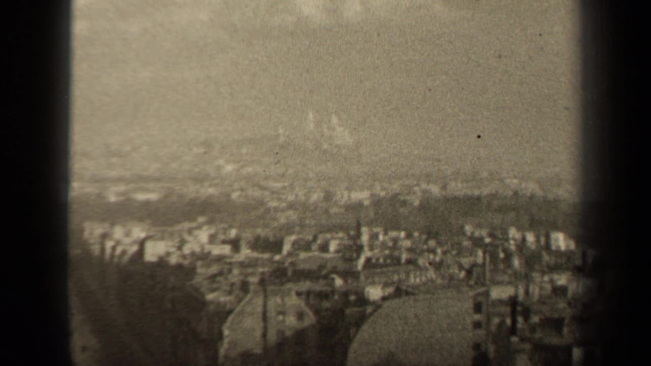 Hazy elevated view of Paris rooftops seen between dark vertical edges.