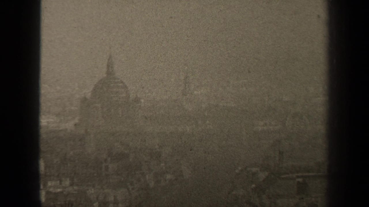 1947 Paris home-movie frame showing a distant domed landmark through haze and dark window bars.