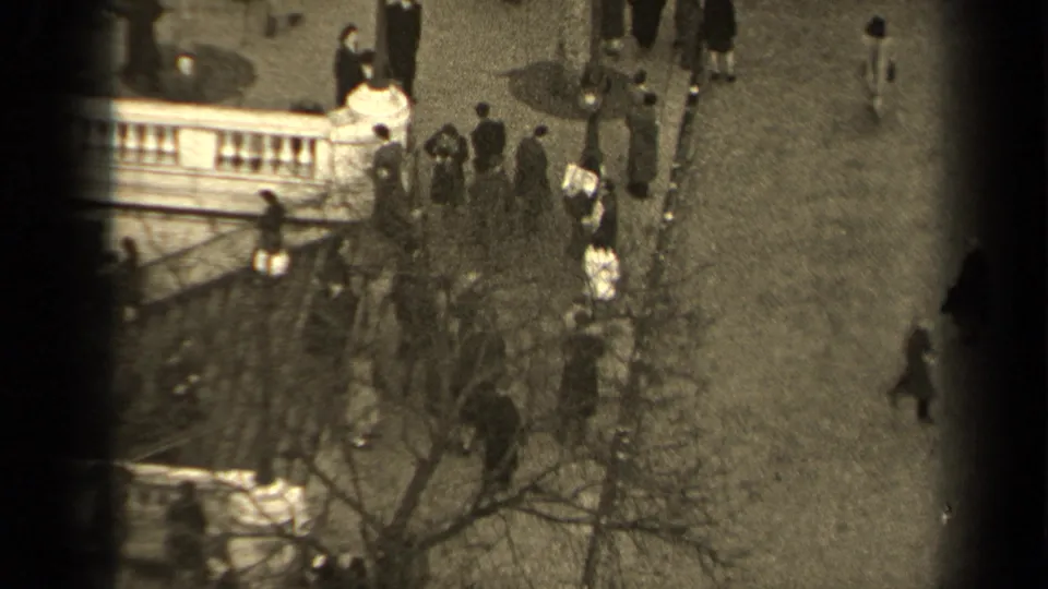 Final 1947 Paris home-movie frame with pedestrians scattered across a cobblestone street near bare trees and a white balustrade.